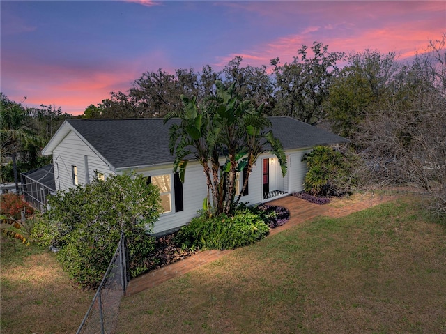 view of front of home featuring glass enclosure, a yard, and roof with shingles