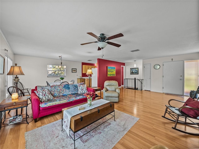 living room featuring light wood finished floors, visible vents, and ceiling fan with notable chandelier