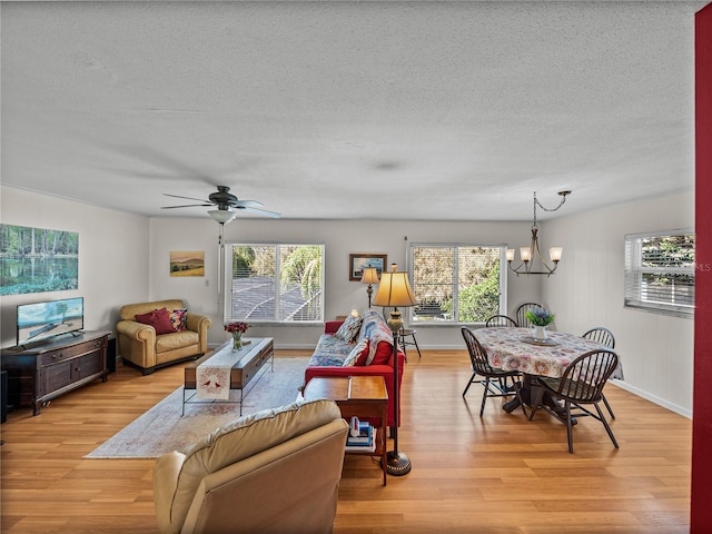 living area featuring plenty of natural light, light wood-style flooring, a textured ceiling, and ceiling fan with notable chandelier