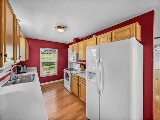 kitchen featuring light countertops, light wood-style flooring, a sink, white appliances, and baseboards