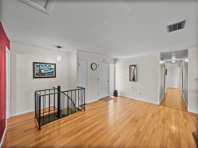 empty room with light wood-type flooring, visible vents, a textured ceiling, and baseboards