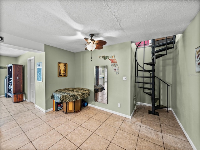 interior space featuring light tile patterned floors, ceiling fan, a textured ceiling, baseboards, and stairs