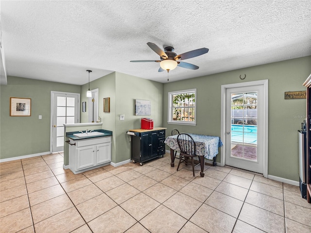 kitchen featuring decorative light fixtures, light tile patterned floors, white cabinets, a sink, and baseboards