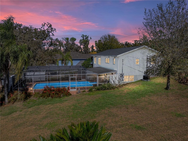 back of house at dusk featuring a lanai, an outdoor pool, and a yard