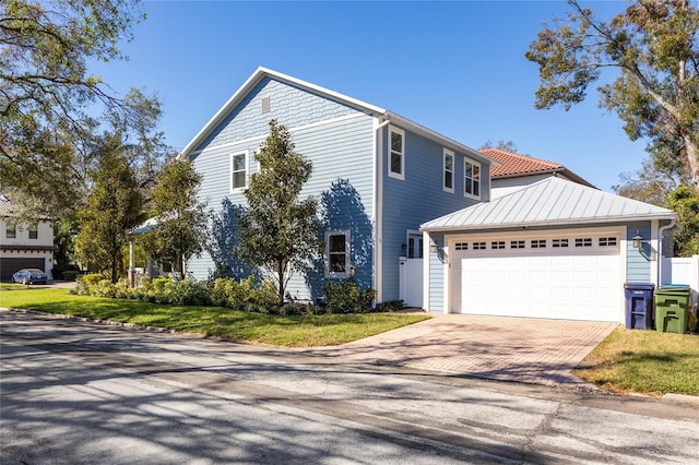 view of front facade featuring decorative driveway, a front yard, a standing seam roof, metal roof, and a garage