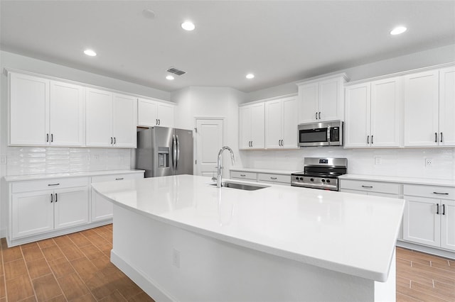 2569 Rogers Rd, Lakeland, FL 33812 - kitchen with appliances with stainless steel finishes, a kitchen island with sink, wood tiled floors, light countertops, and white cabinetry