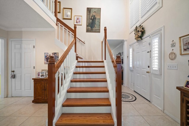 foyer entrance with light tile patterned floors, ornamental molding, stairs, and a towering ceiling