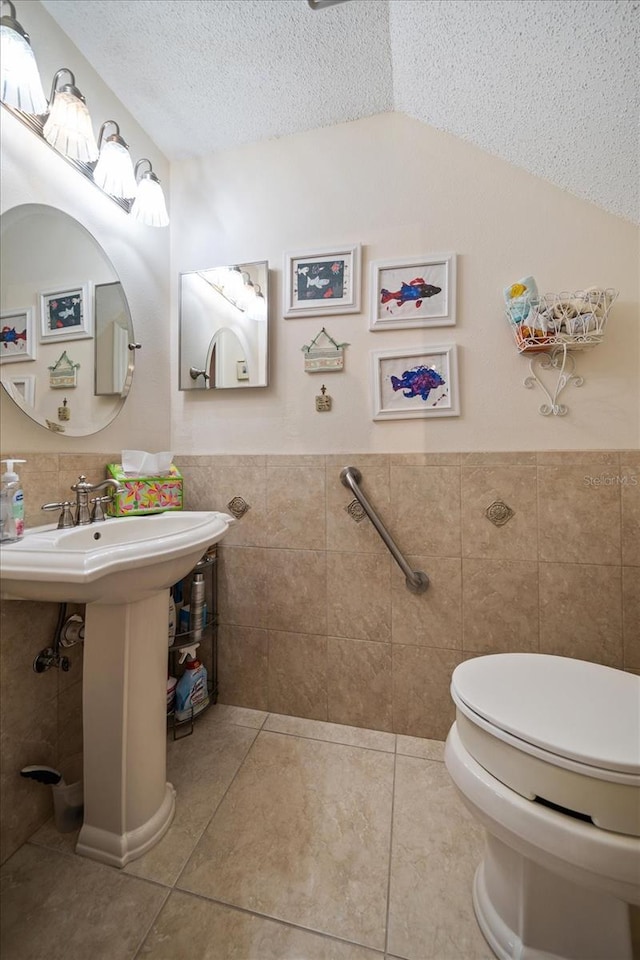 half bathroom featuring a textured ceiling, toilet, tile walls, vaulted ceiling, and tile patterned floors