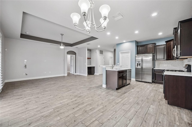 kitchen featuring a center island with sink, a raised ceiling, appliances with stainless steel finishes, open floor plan, and light countertops