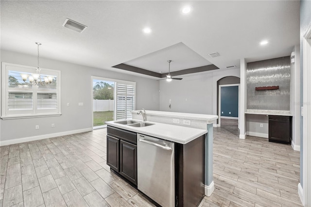 kitchen featuring dishwasher, a kitchen island with sink, a tray ceiling, light countertops, and a sink