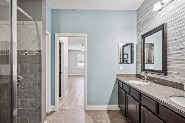 bathroom featuring double vanity, tiled shower, a sink, and baseboards