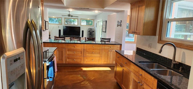 kitchen with ceiling fan, concrete floors, a sink, appliances with stainless steel finishes, and dark stone countertops