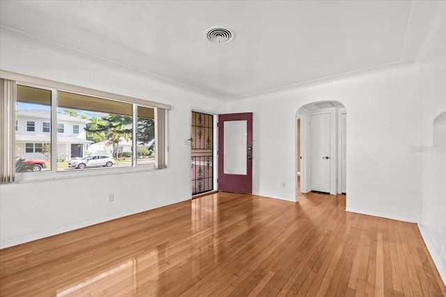 empty room with arched walkways, wood-type flooring, visible vents, and baseboards