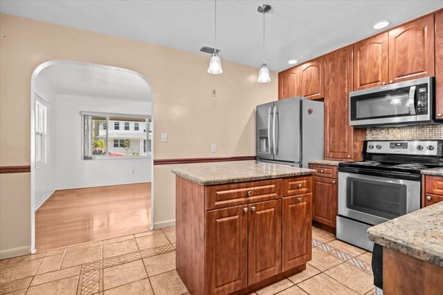 kitchen with arched walkways, a kitchen island, appliances with stainless steel finishes, light stone countertops, and pendant lighting