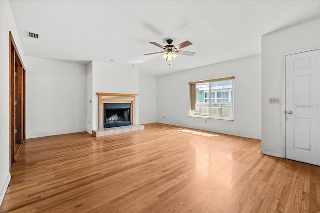 unfurnished living room with visible vents, a fireplace with raised hearth, light wood-style floors, a ceiling fan, and baseboards