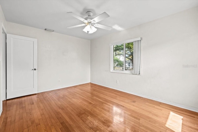 empty room featuring light wood-style flooring, a ceiling fan, visible vents, and baseboards