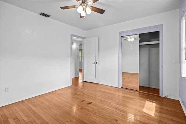 unfurnished bedroom featuring arched walkways, light wood finished floors, a closet, visible vents, and baseboards