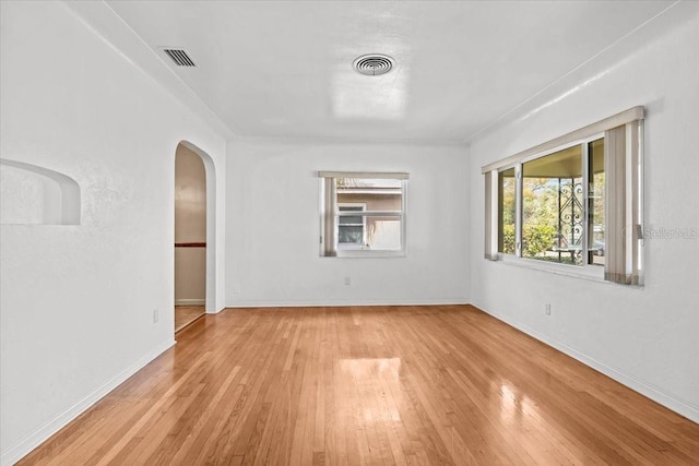 unfurnished room with arched walkways, light wood-type flooring, visible vents, and baseboards