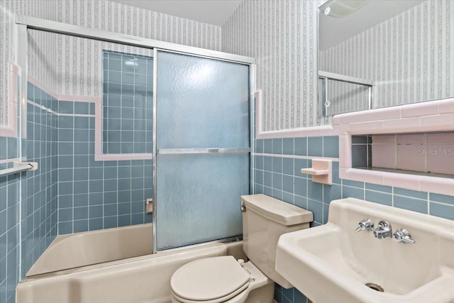 full bathroom featuring enclosed tub / shower combo, toilet, a sink, wainscoting, and wallpapered walls