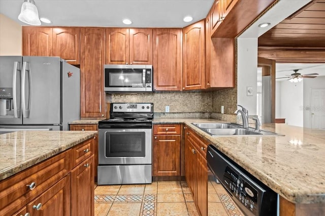 kitchen with light stone counters, brown cabinets, stainless steel appliances, decorative backsplash, and a sink