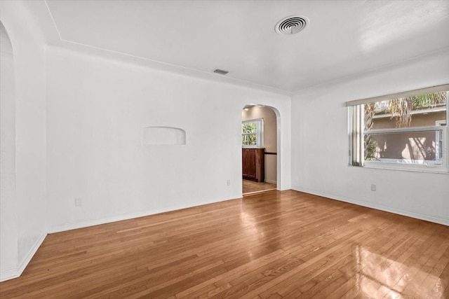 empty room featuring hardwood / wood-style flooring, visible vents, arched walkways, and baseboards