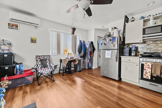 kitchen featuring stainless steel appliances, a wall mounted air conditioner, light wood-style flooring, and white cabinetry