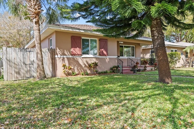 ranch-style house featuring a front yard, fence, and stucco siding