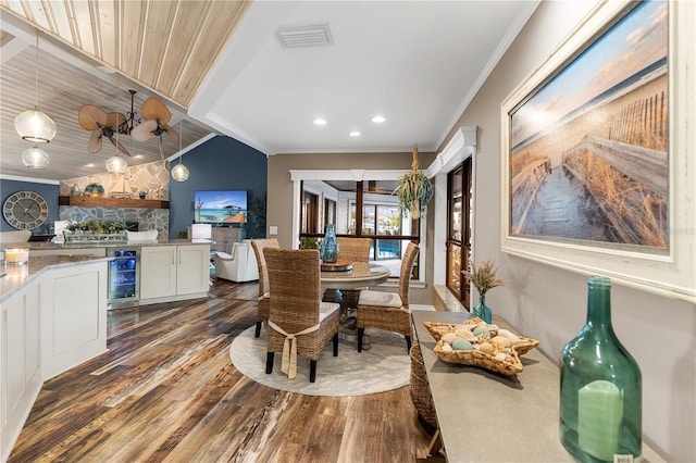 dining room with visible vents, beverage cooler, wood finished floors, crown molding, and vaulted ceiling