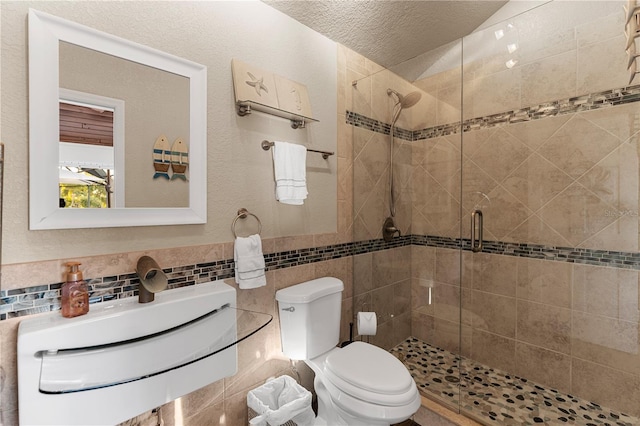 bathroom with toilet, a stall shower, a sink, a textured ceiling, and tile walls