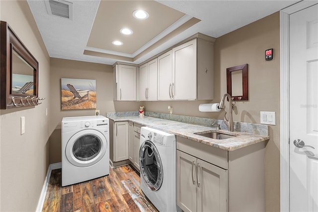 laundry room featuring washing machine and clothes dryer, visible vents, wood finished floors, cabinet space, and a sink