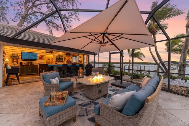 view of patio with glass enclosure, an outdoor living space with a fire pit, and a water view