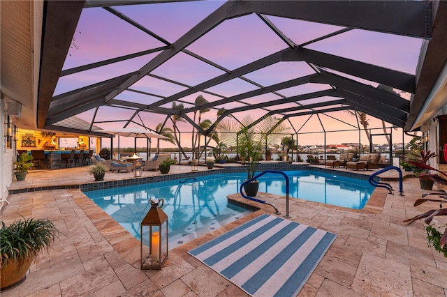 pool at dusk with an outdoor pool, a patio, and a lanai