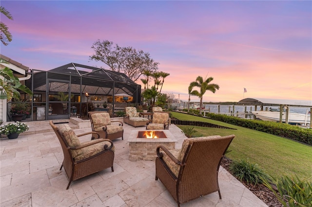 patio terrace at dusk with a yard, a water view, glass enclosure, and an outdoor fire pit