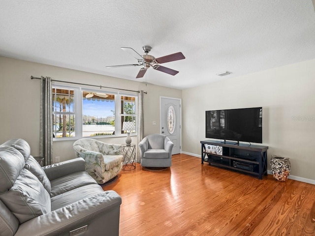 living room featuring visible vents, baseboards, a ceiling fan, wood finished floors, and a textured ceiling