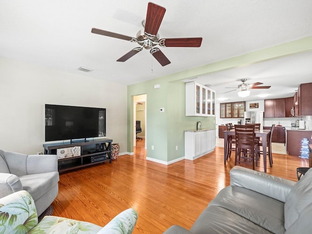 living area with baseboards, a ceiling fan, visible vents, and light wood-style floors