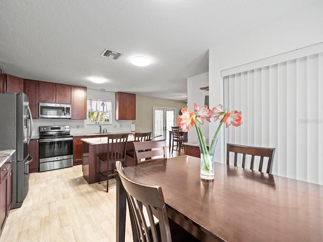 dining room with light wood-style flooring, visible vents, a textured ceiling, and french doors