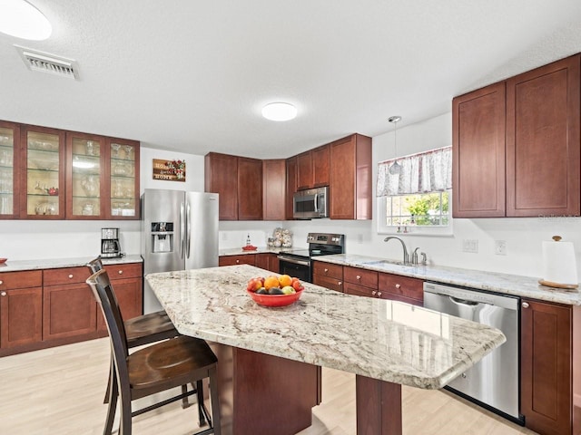 kitchen featuring visible vents, a kitchen island, decorative light fixtures, stainless steel appliances, and a kitchen bar