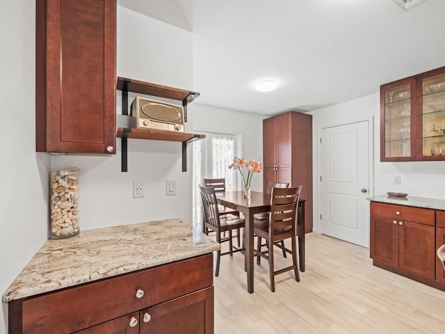 kitchen featuring open shelves, light wood finished floors, glass insert cabinets, and light stone countertops