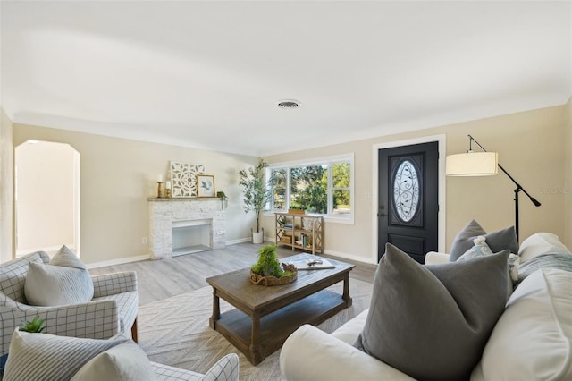 living room featuring a stone fireplace and light wood-type flooring