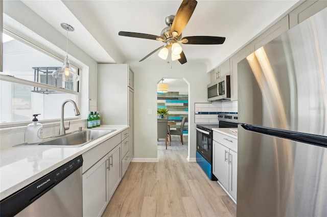 kitchen featuring appliances with stainless steel finishes, light hardwood / wood-style flooring, tasteful backsplash, decorative light fixtures, and sink