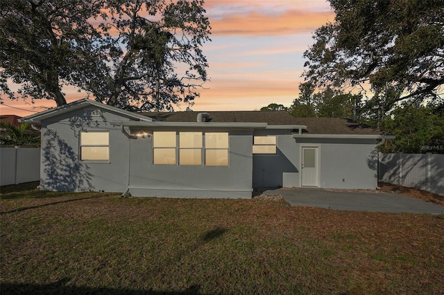 back house at dusk featuring a patio and a yard