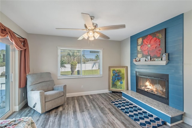 living area with a large fireplace, ceiling fan, wood finished floors, and baseboards