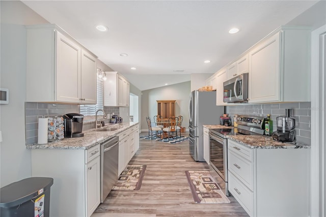 kitchen with a sink, white cabinets, vaulted ceiling, appliances with stainless steel finishes, and light wood-type flooring