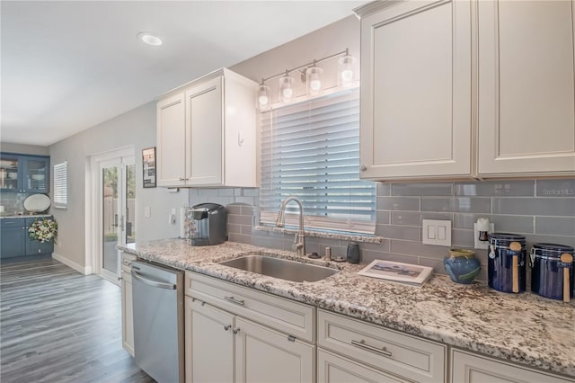 kitchen with dishwasher, light stone counters, backsplash, light wood-type flooring, and a sink