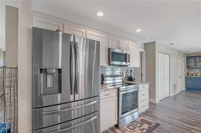 kitchen featuring visible vents, appliances with stainless steel finishes, wood finished floors, light stone countertops, and backsplash