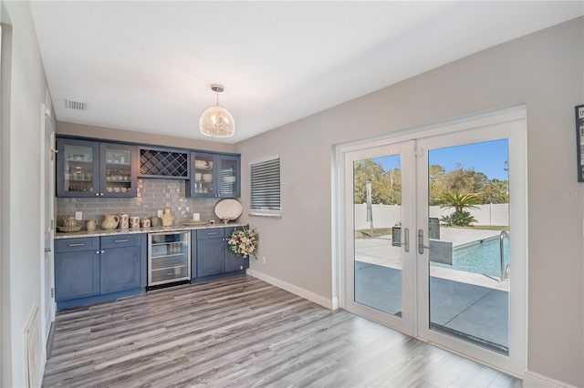 bar featuring wine cooler, indoor bar, baseboards, backsplash, and light wood finished floors