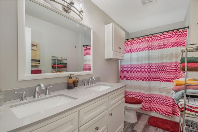 full bathroom with toilet, double vanity, a sink, and visible vents