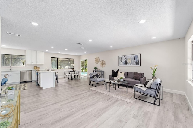 living room featuring a textured ceiling, light wood-type flooring, visible vents, and recessed lighting