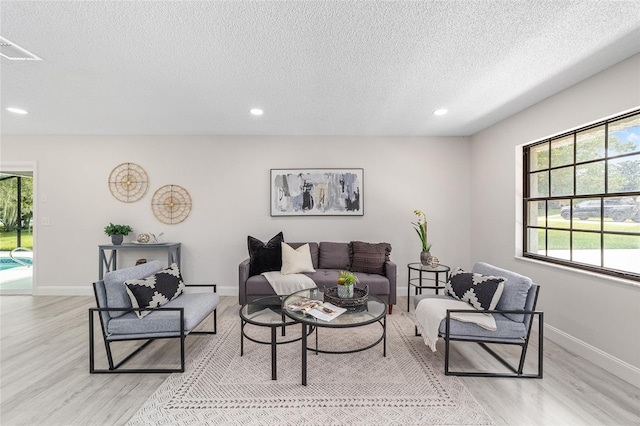 living room with a textured ceiling, recessed lighting, light wood-style flooring, and baseboards