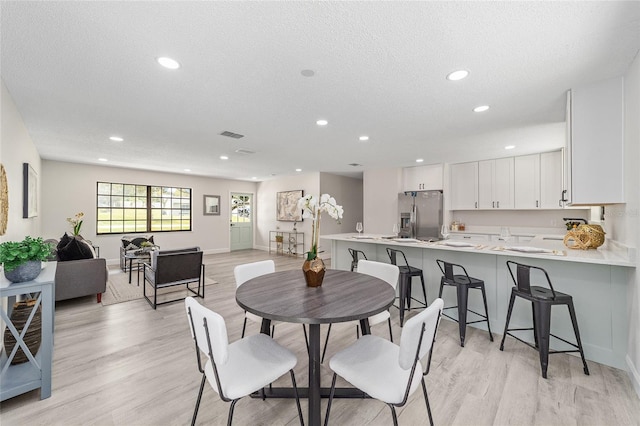 dining room featuring light wood-style floors, baseboards, a textured ceiling, and recessed lighting